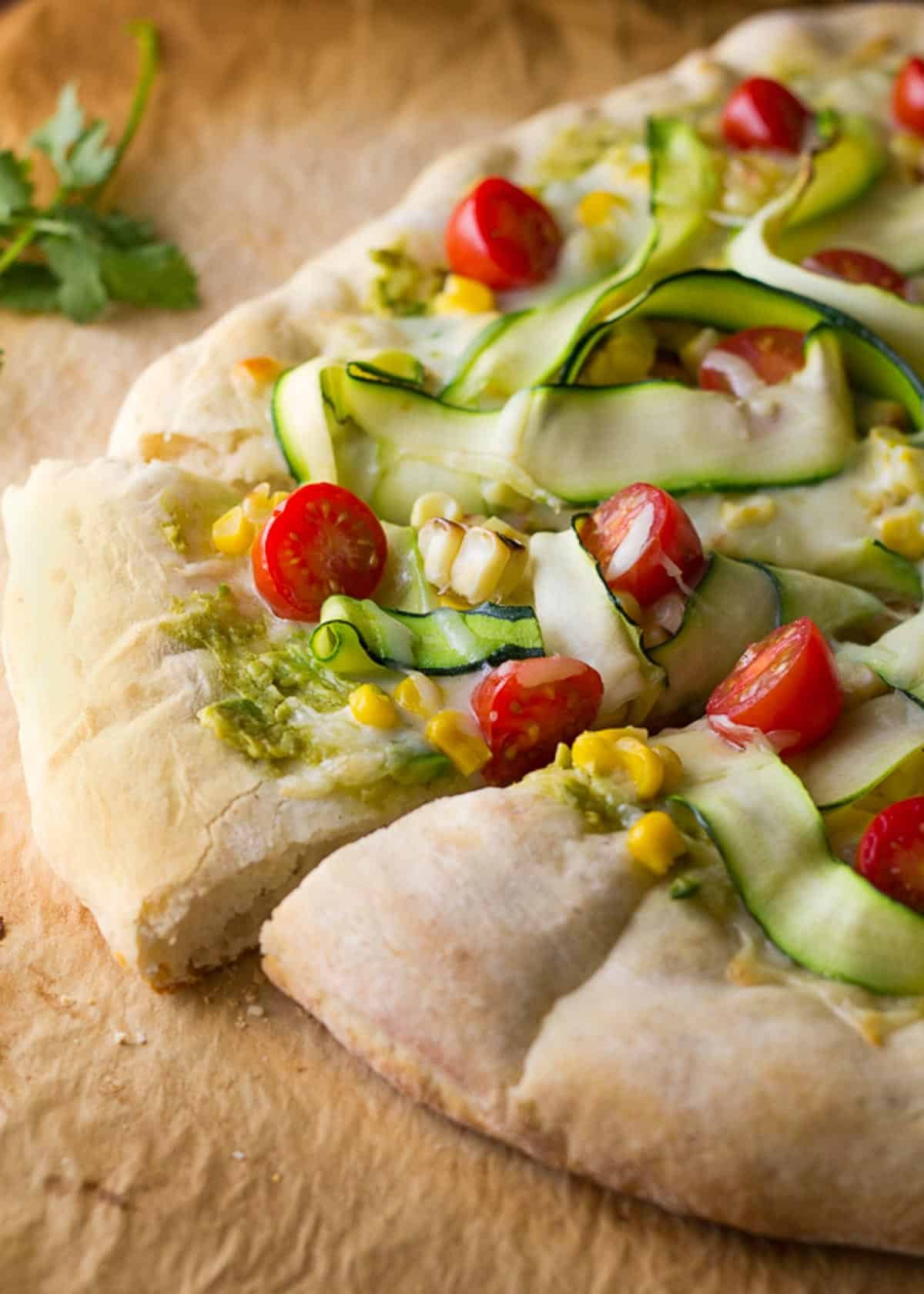 a flatbread pizza topped with avocado, corn, zucchini, tomatoes, and mozzarella cheese