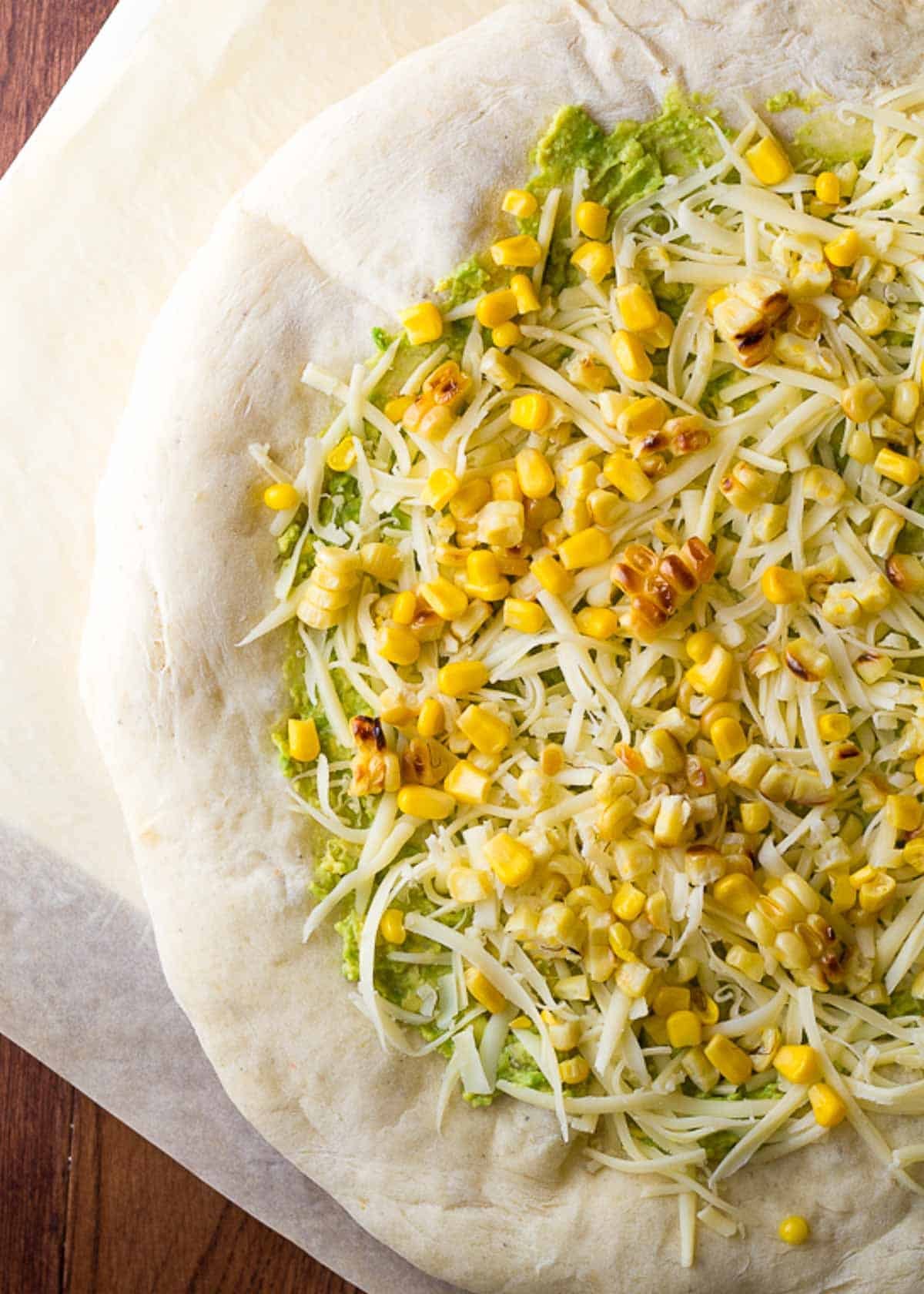 parbaked pizza dough topped with avocado mash, shredded mozzarella, and charred corn