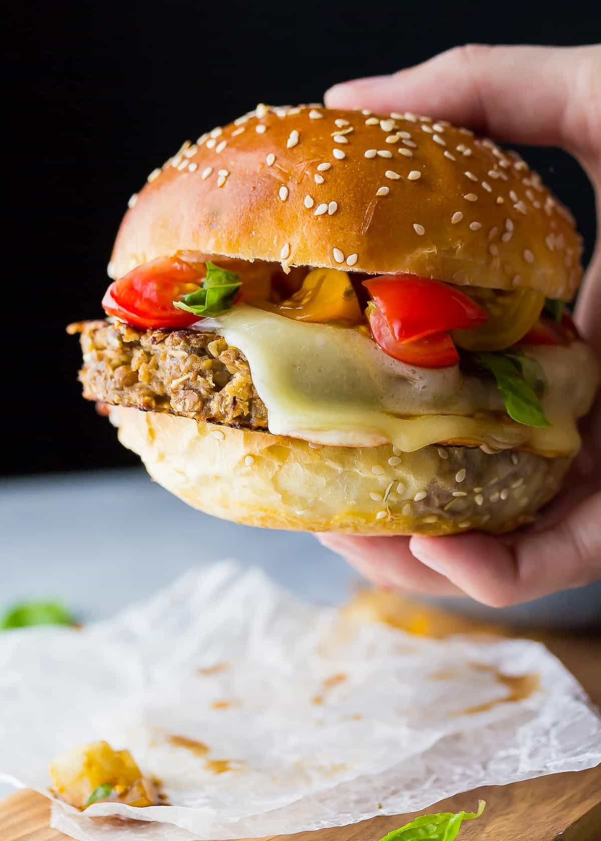 a hand holding a veggie burger topped with mozzarella and a tomato bruschetta