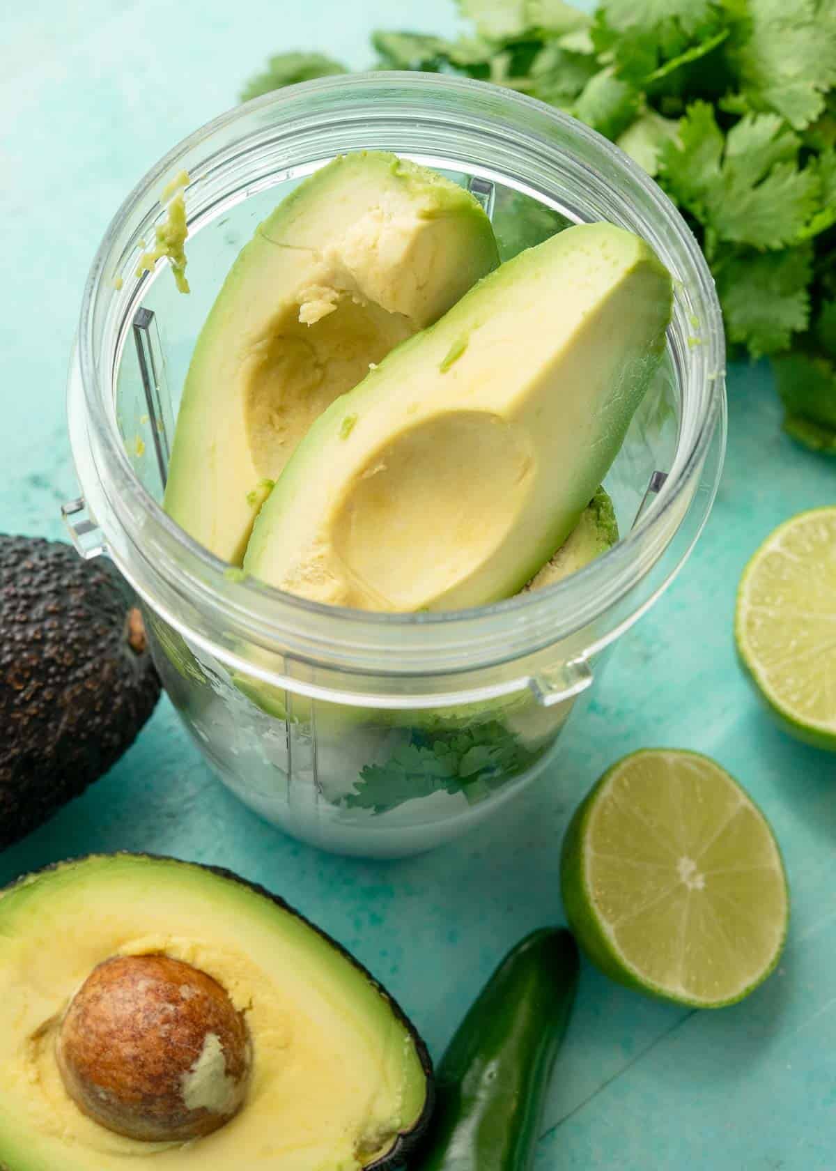 a blender full of avocado, sour cream, cilantro, cumin, onion, jalapeno, and garlic
