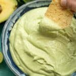 a chip being dipped into a thick avocado crema with cilantro lime flavor