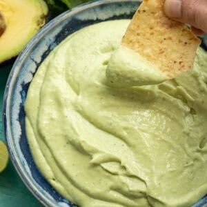 a chip being dipped into a thick avocado crema with cilantro lime flavor