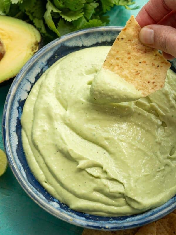 a chip being dipped into a thick avocado crema with cilantro lime flavor