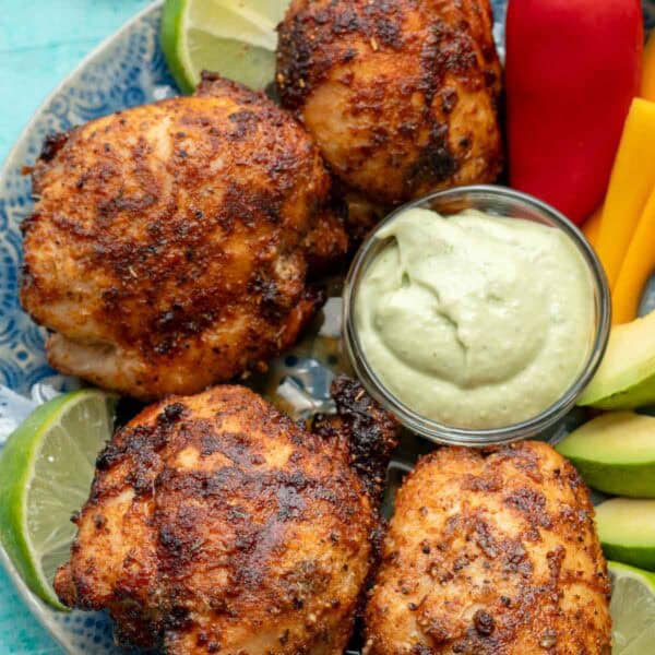 overhead shot showing a platter of air fryer boneless chicken thighs, veggies, avocado crema, and lime wedges