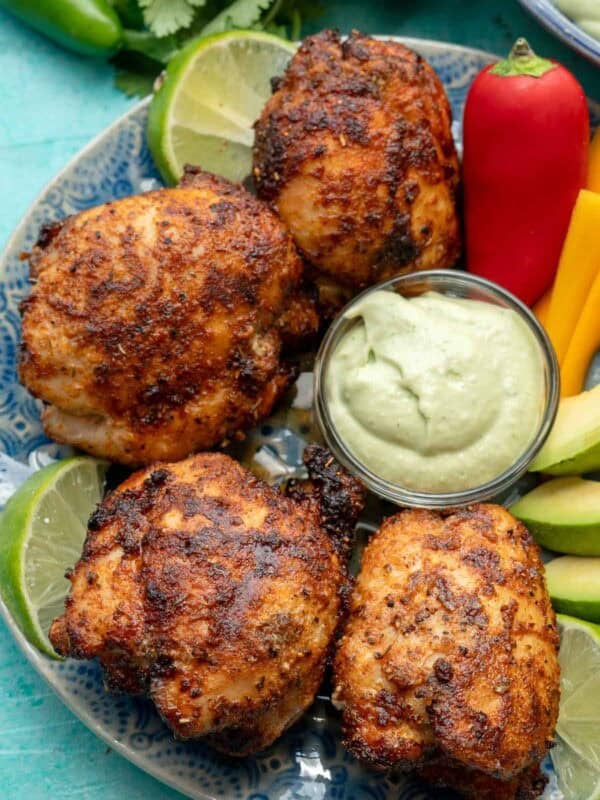 overhead shot showing a platter of air fryer boneless chicken thighs, veggies, avocado crema, and lime wedges