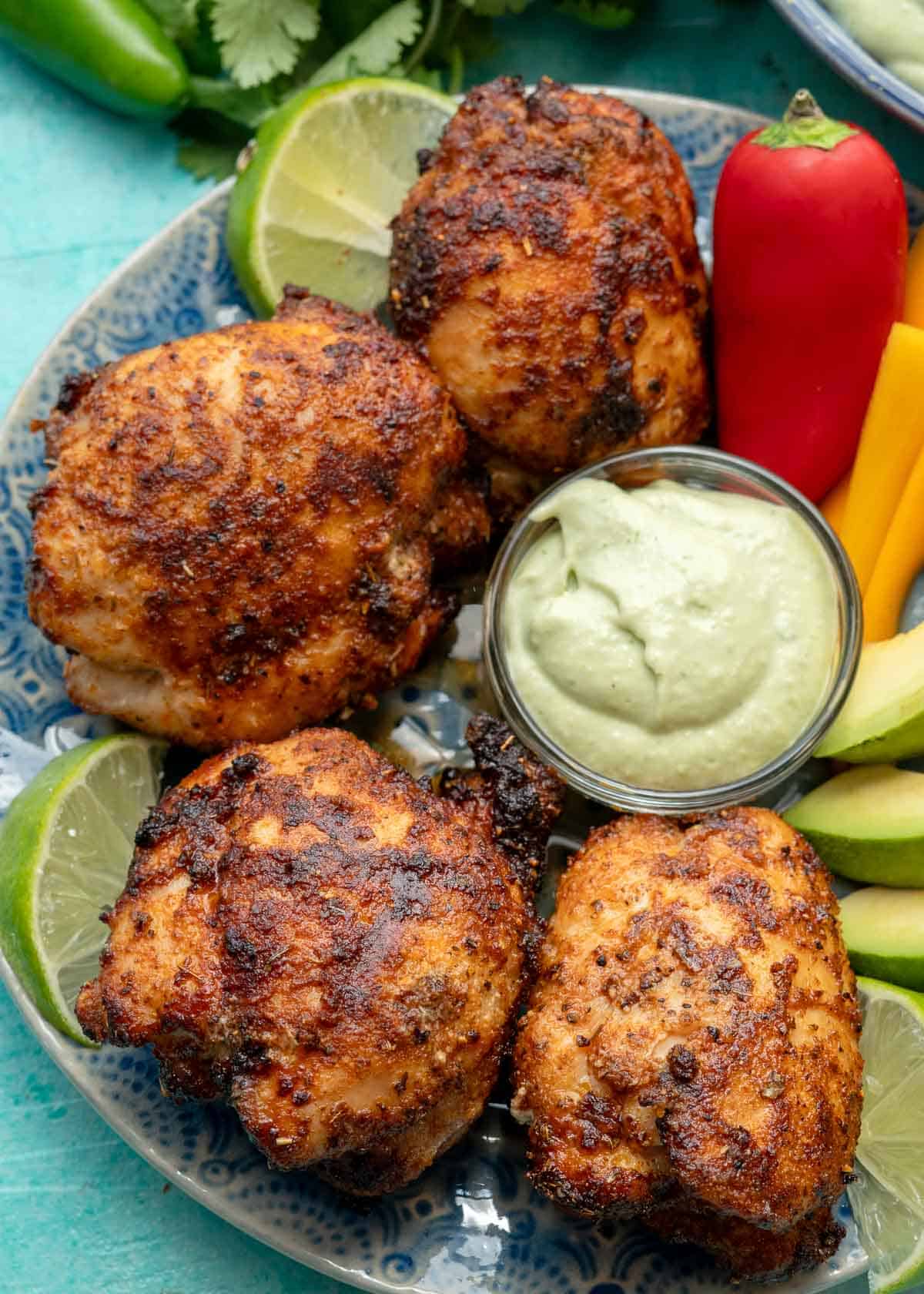 overhead shot showing a platter of air fryer boneless chicken thighs, veggies, avocado crema, and lime wedges