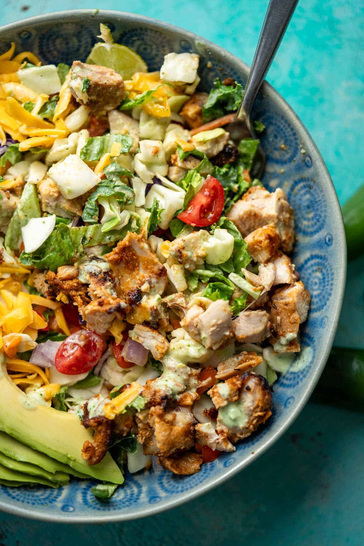 a mixed taco salad with juicy chicken, jalapeno ranch, and sliced avocado in a bowl with a fork