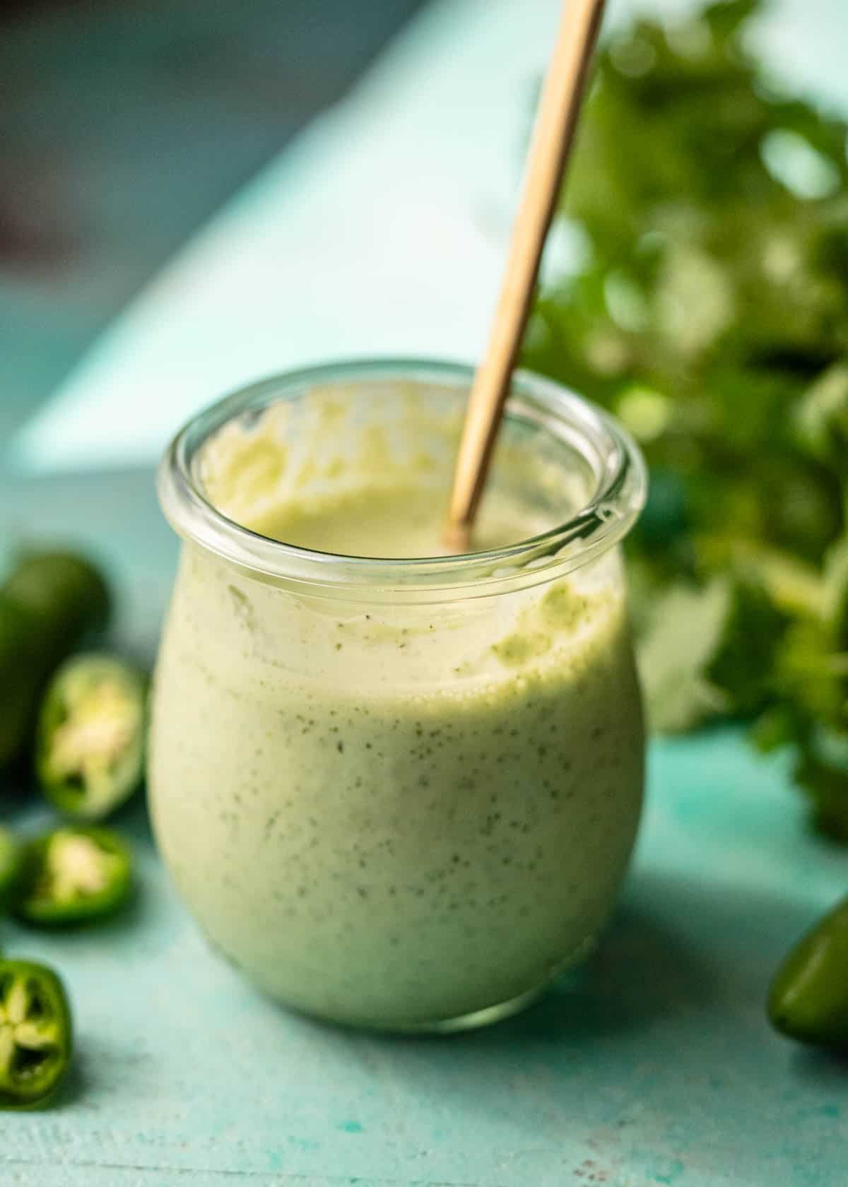 a jar of jalapeno ranch surrounded with chopped jalapenos and fresh cilantro