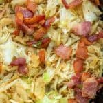 a cast iron skillet full of fried cabbage and crispy bacon with tender onions