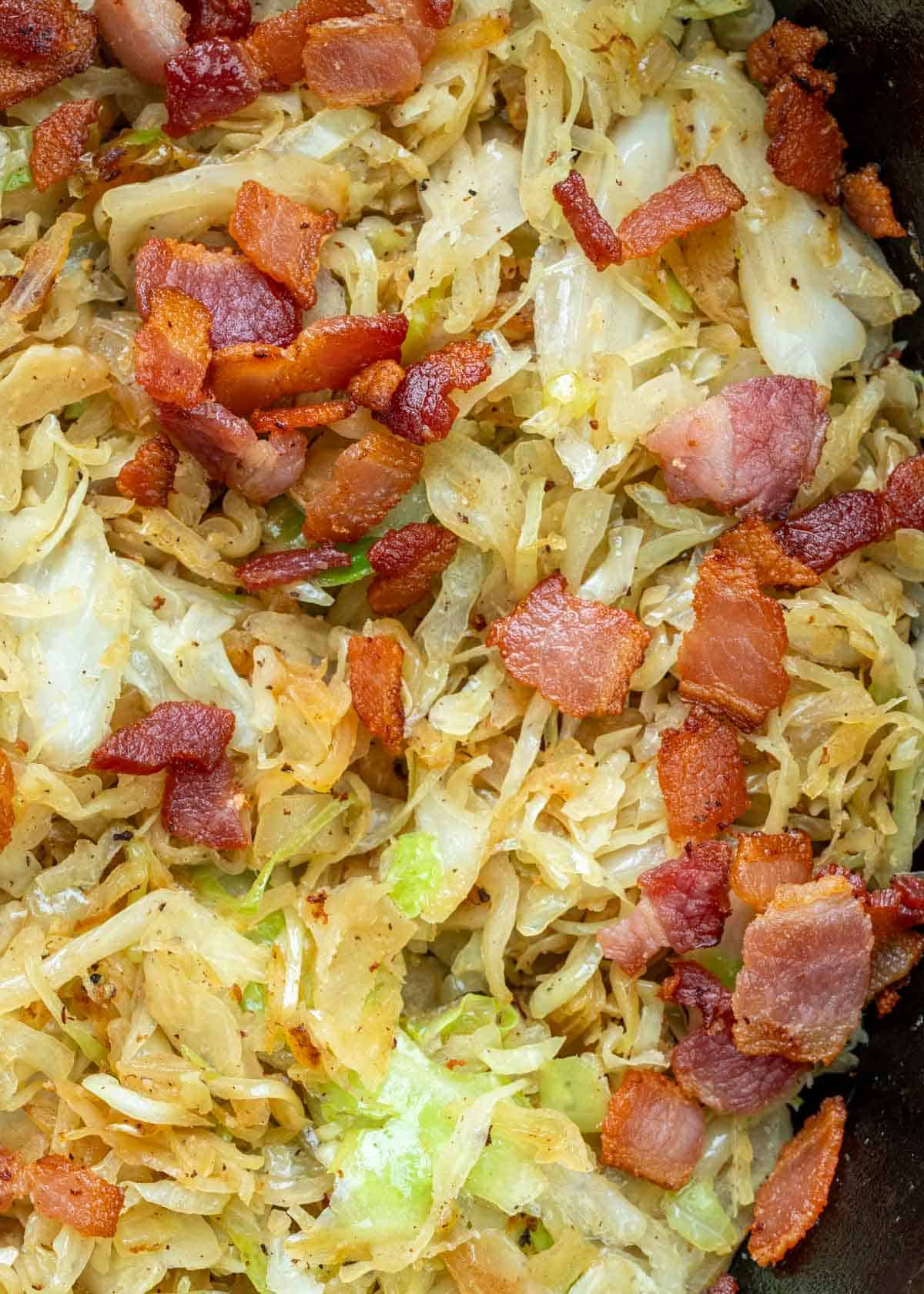 a cast iron skillet full of fried cabbage and crispy bacon with tender onions