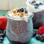 two jars of blueberry chia pudding on a counter surrounded with fruit