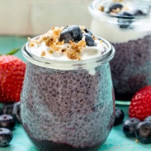 two jars of blueberry chia pudding on a counter surrounded with fruit