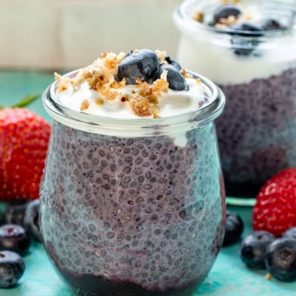 two jars of blueberry chia pudding on a counter surrounded with fruit