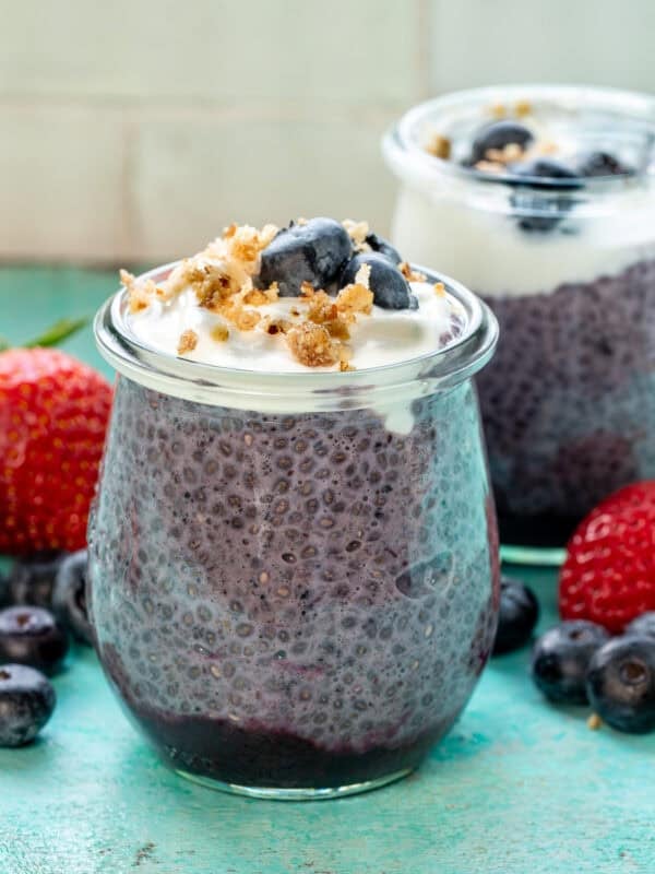 two jars of blueberry chia pudding on a counter surrounded with fruit