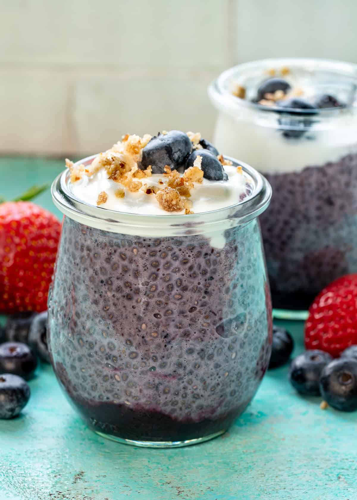 two jars of blueberry chia pudding on a counter surrounded with fruit
