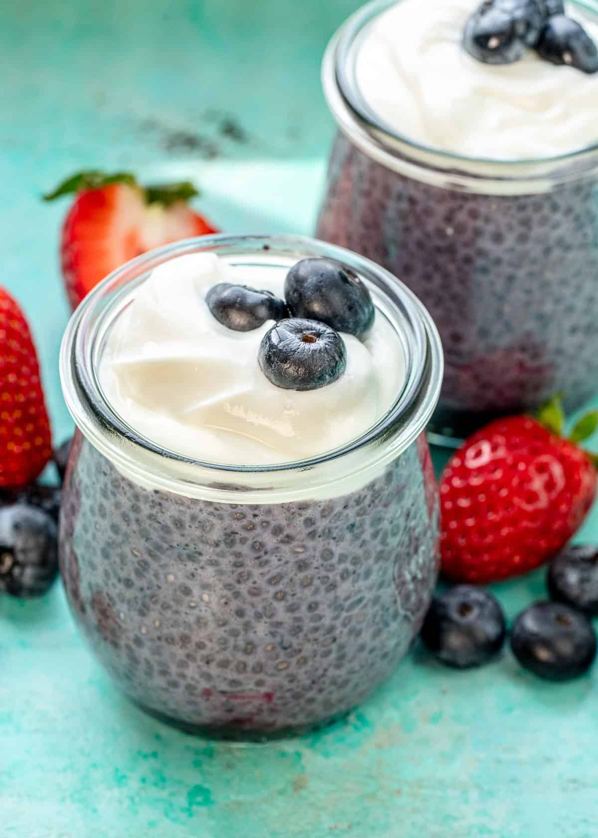 two chia blueberry pudding jars on a counter with berries