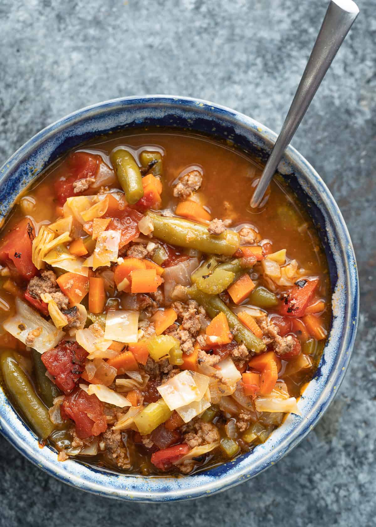 overhead image of hamburger soup with cabbage in a blue bowl with a spoon