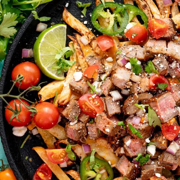 a plate loaded with carne asada on rutabaga fries and loaded with tomatoes, cilantro, cheese, and jalapenoes