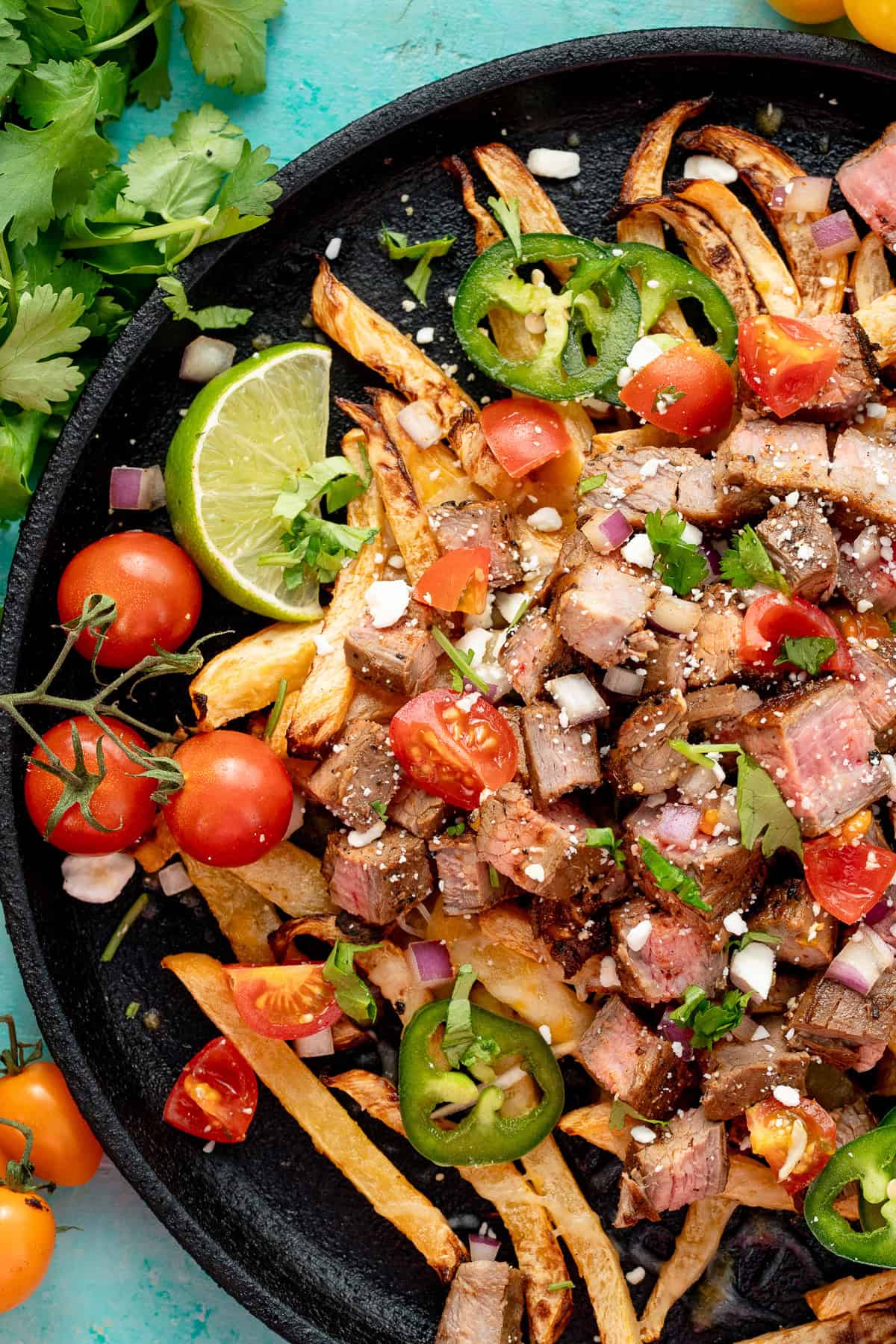 a skillet loaded with carne asada on rutabaga fries and loaded with tomatoes, cilantro, cheese, and jalapenoes