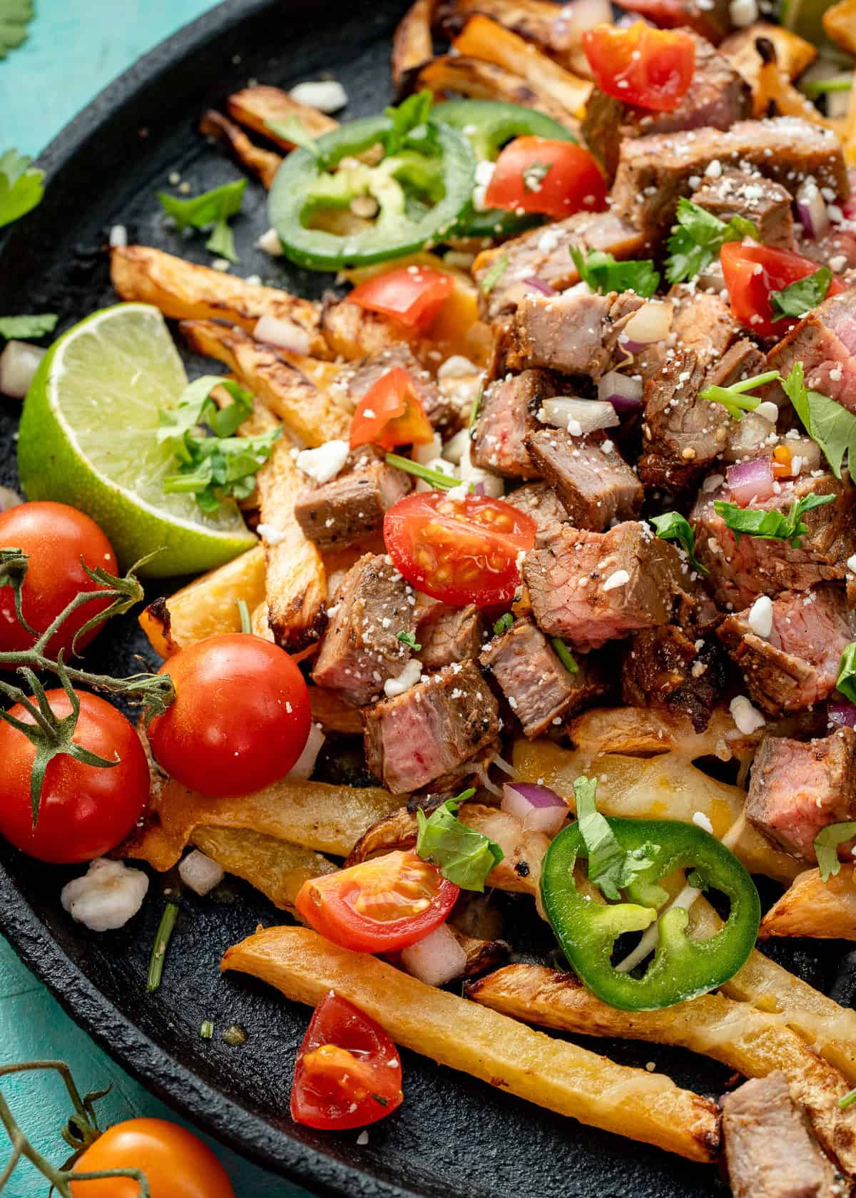 tomatoes, jalapenos, cilantro, and cheese atop a plate of the best carne asada fries
