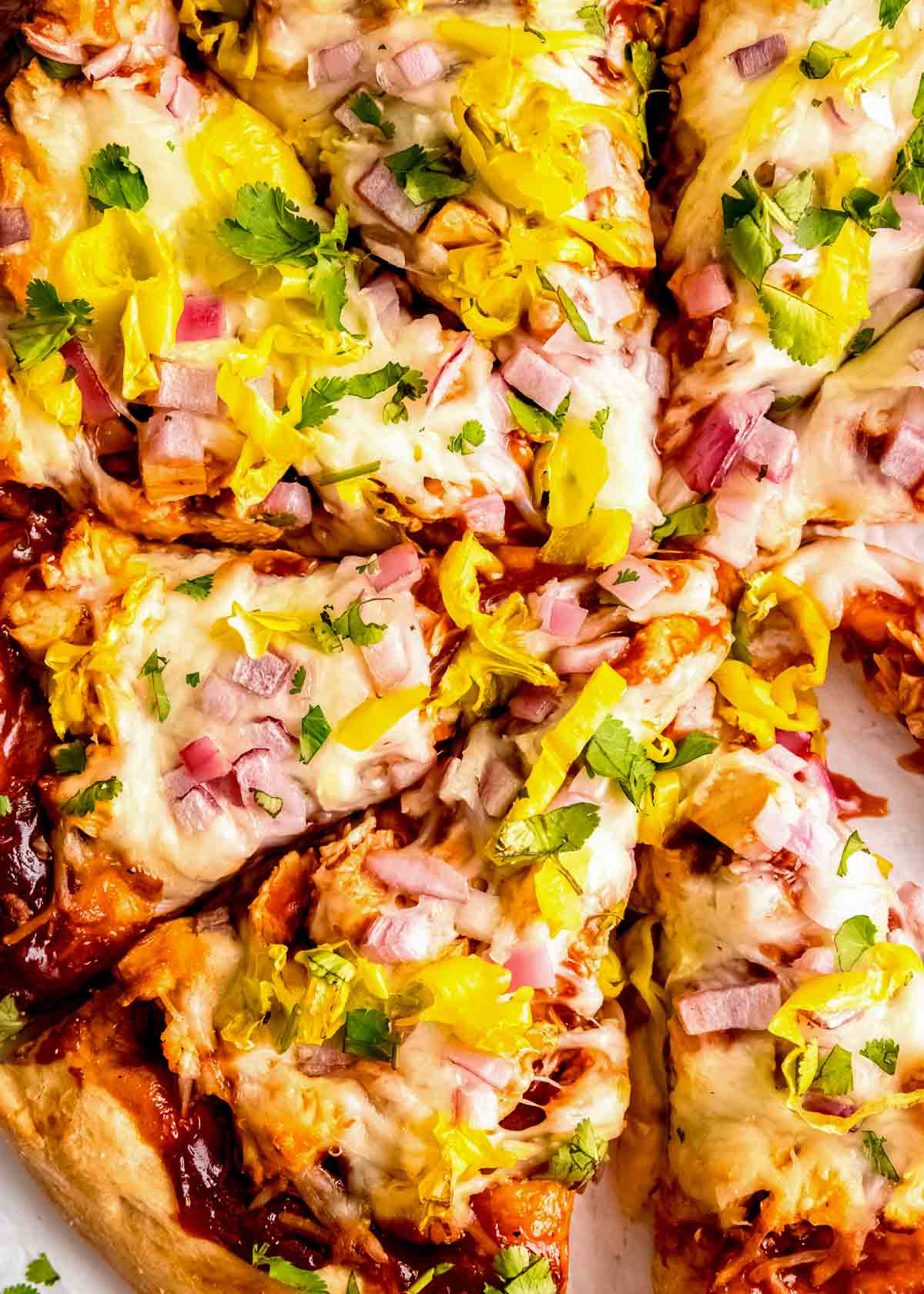 center shot of barbecue chicken pizza cut into slices with melty mozzarella, cilantro, red onions, and pepperoncini on top