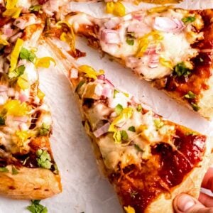 a hand grabbing a cheesy slice of homemade bbq chicken pizza