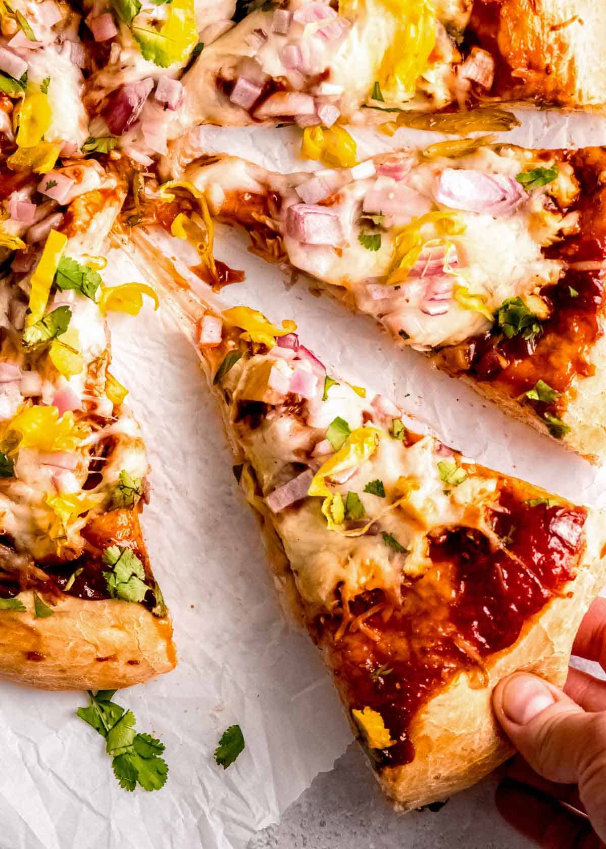a hand grabbing a cheesy slice of homemade bbq chicken pizza
