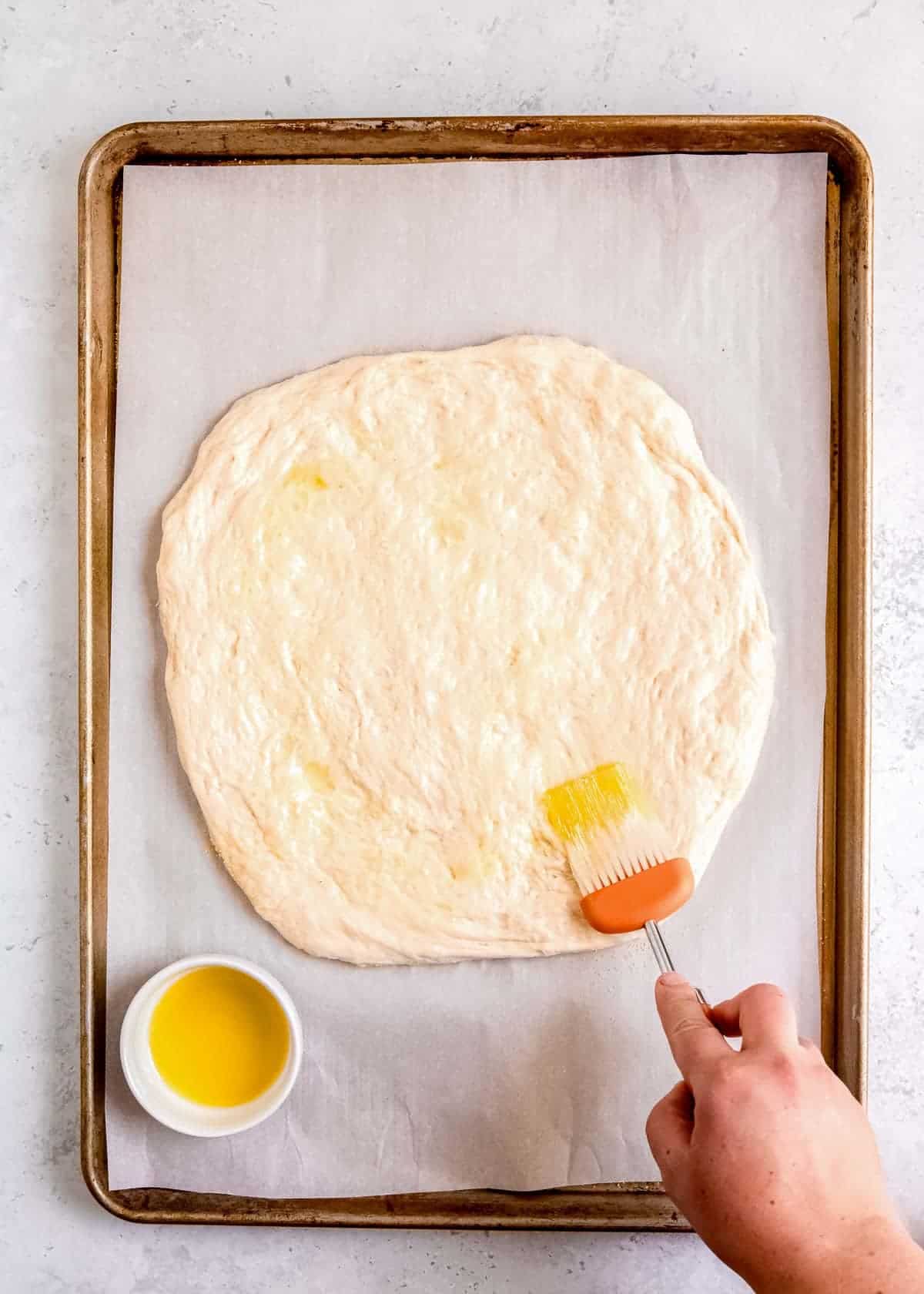 a hand brushing pizza dough with olive oil
