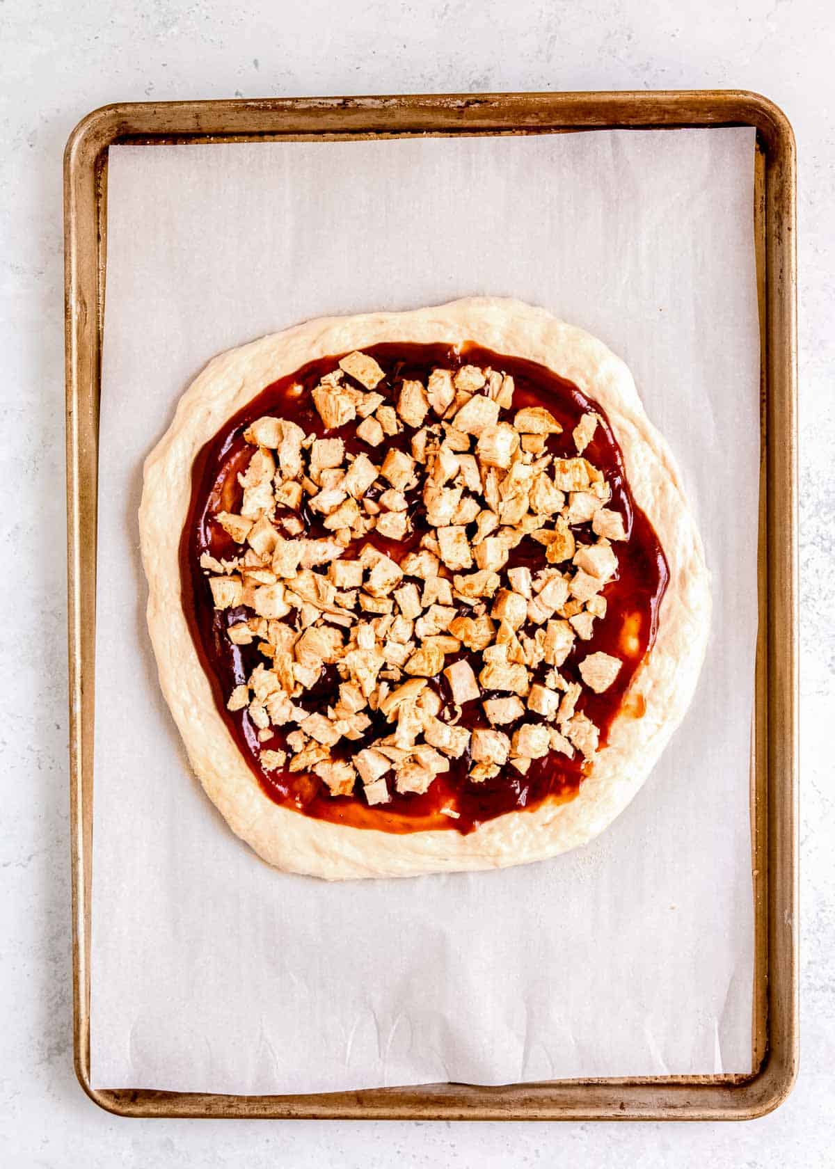 pizza dough covered in bbq sauce and cooked chicken