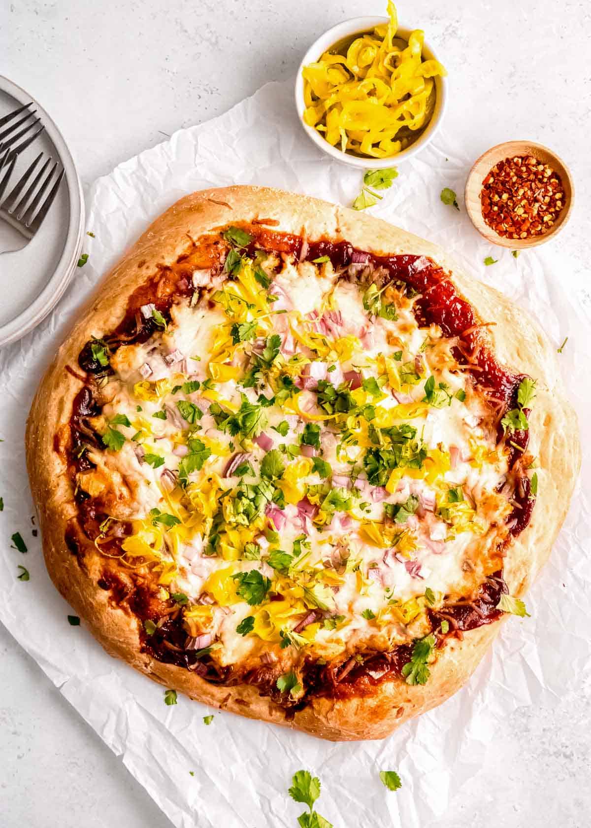 overhead shot showing a barbecue chicken pizza with a side of pepperoncini