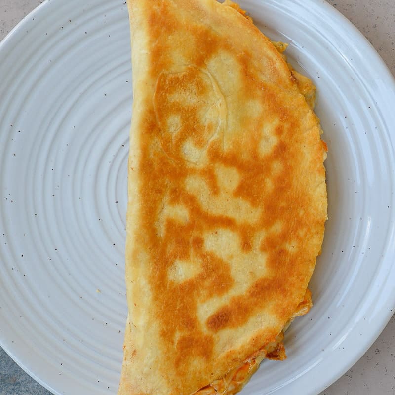 a folded, cooked buffalo chicken quesadilla on a white plate