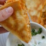 a slice of buffalo chicken quesadilla being dipped in sauce in a white bowl