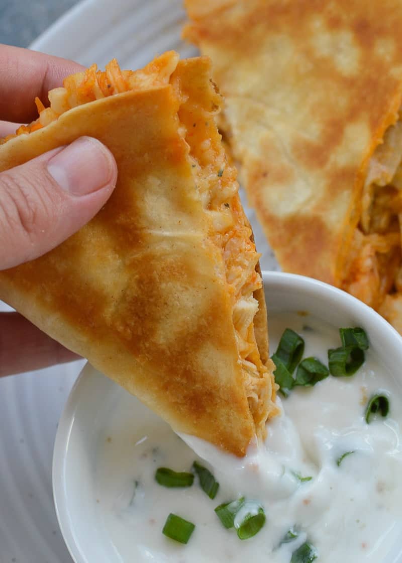 a slice of buffalo chicken quesadilla being dipped in sauce in a white bowl