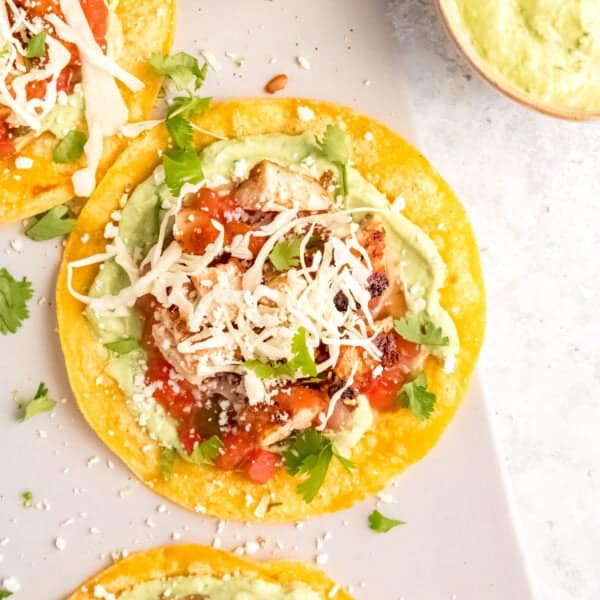 closeup of chicken tostada topped with cheese, salsa, cilantro, and avocado crema