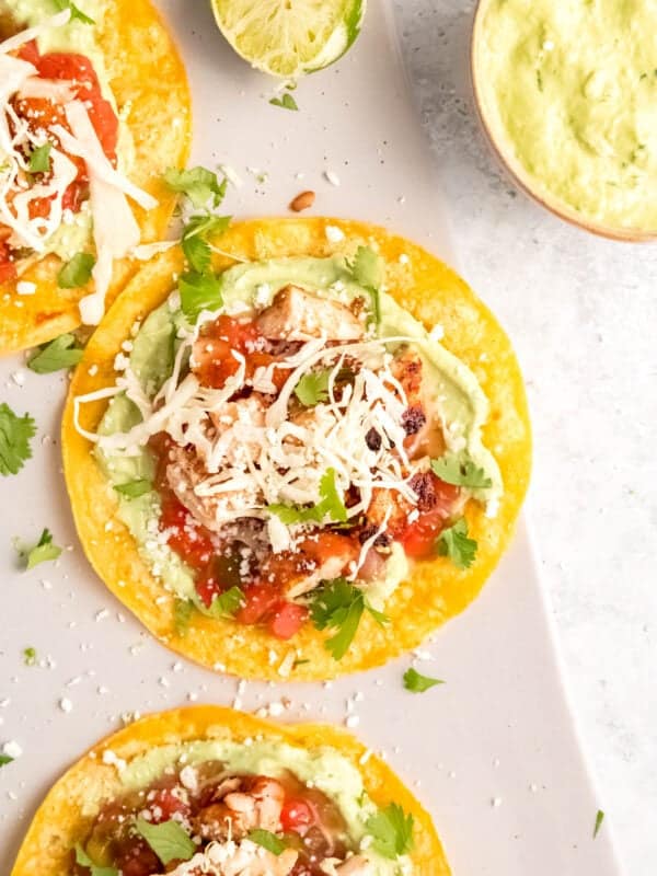 closeup of chicken tostada topped with cheese, salsa, cilantro, and avocado crema