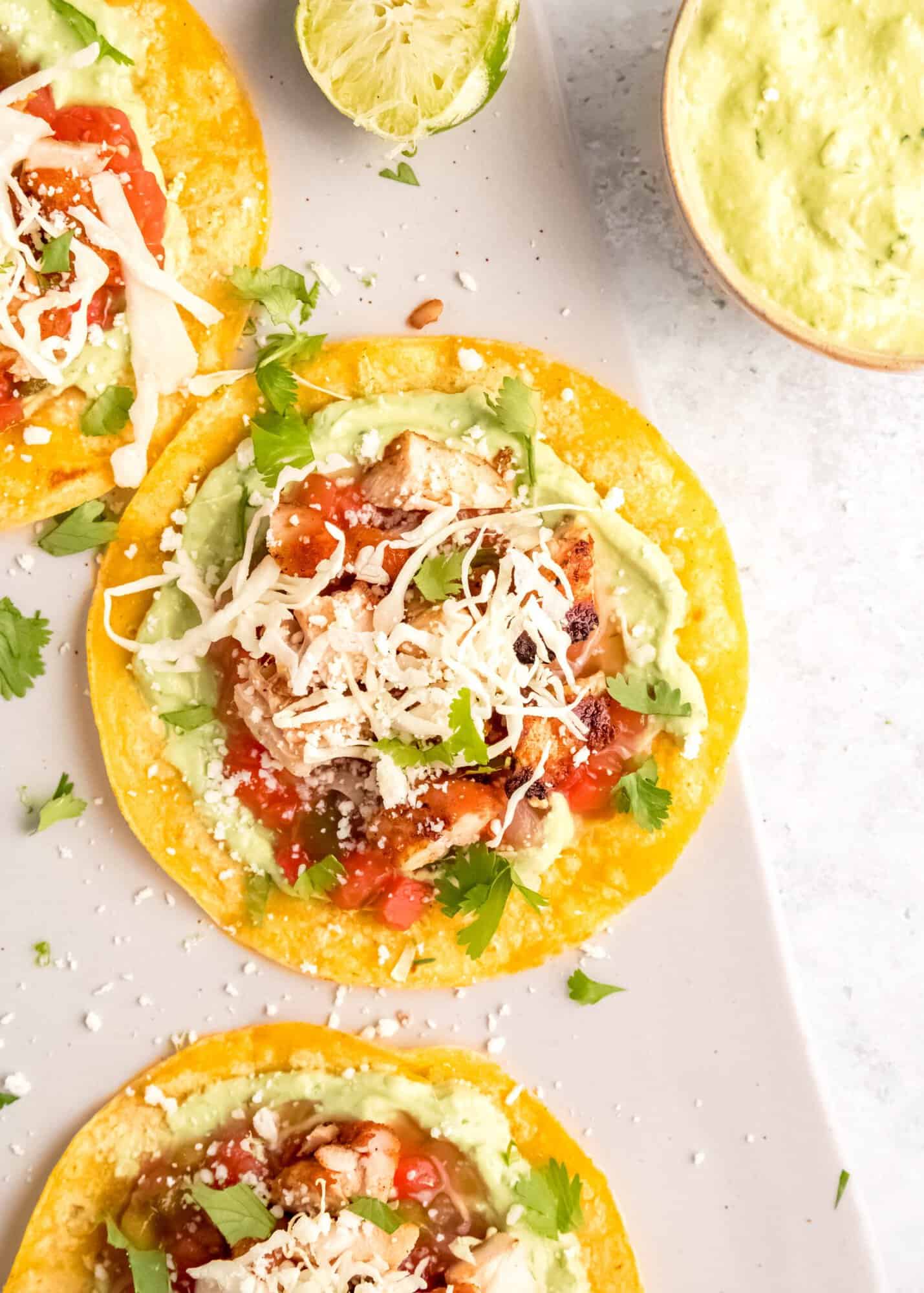 closeup of chicken tostada topped with cheese, salsa, cilantro, and avocado crema