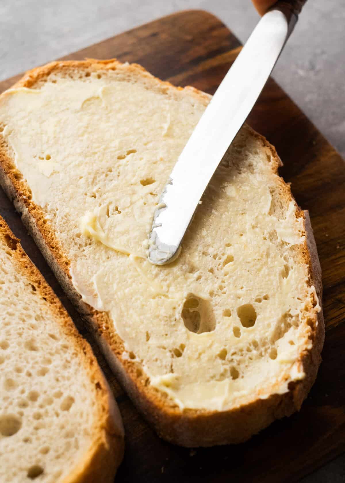bread being buttered on cutting board