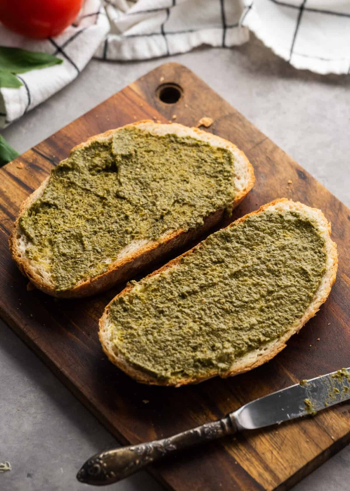 pesto being spread onto bread on cutting board
