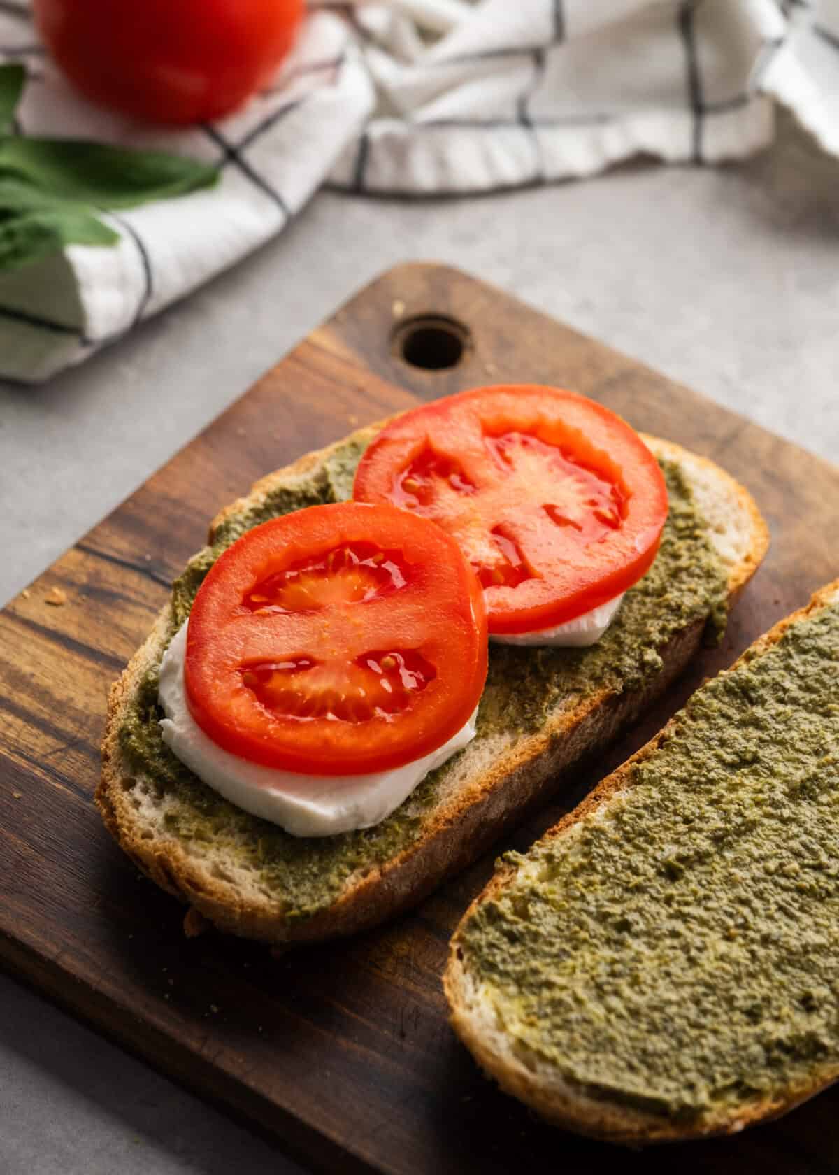 tomatoes and cheese being added to bread on cutting board