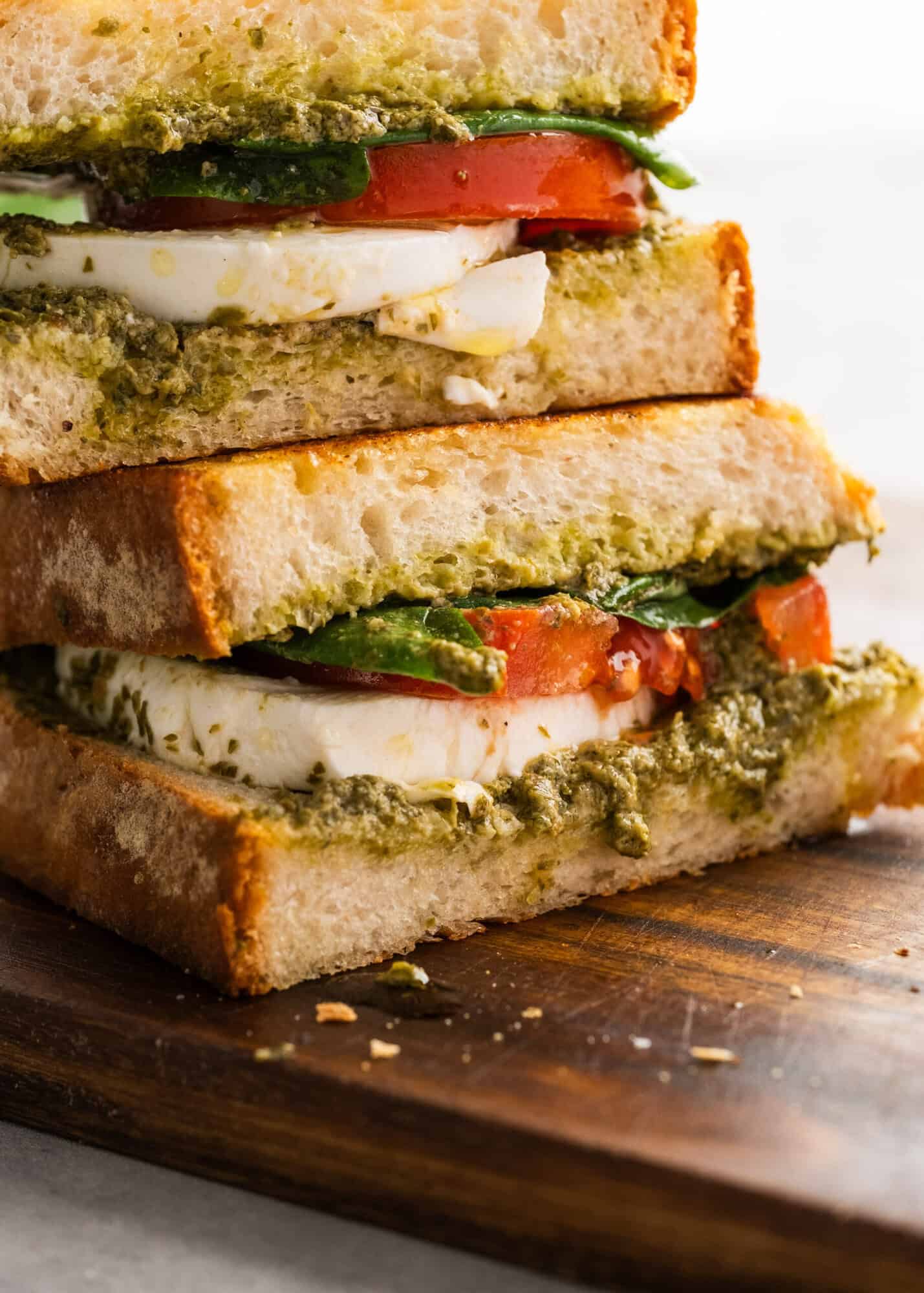 close image of two pesto sandwiches stacked on a cutting board