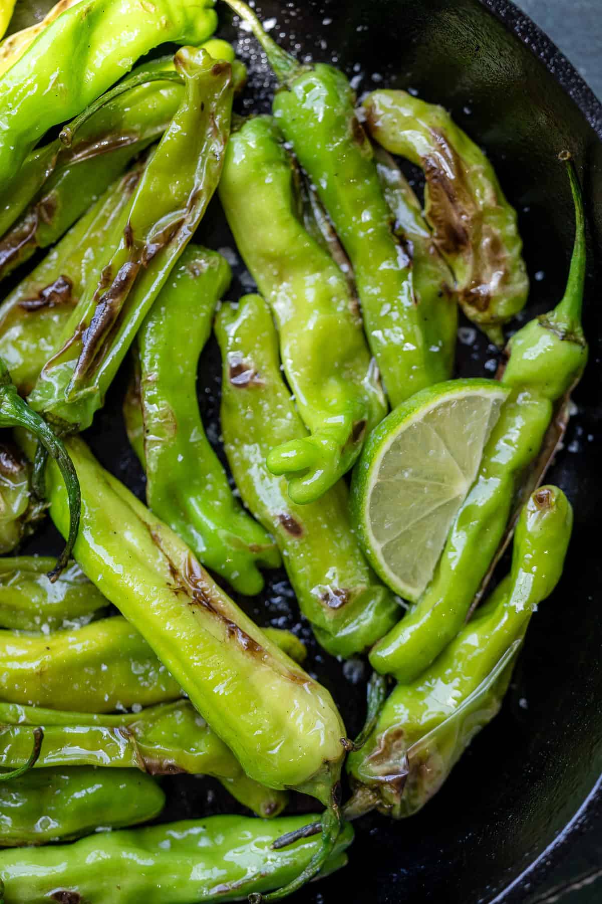 cast iron skillet with blistered shishito peppers with lime wedge
