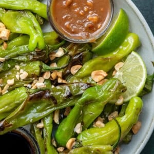 a plate full of perfectly blistered shishito peppers with peanut sauce
