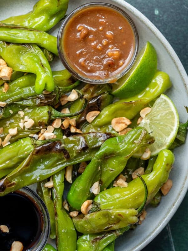 a plate full of perfectly blistered shishito peppers with peanut sauce