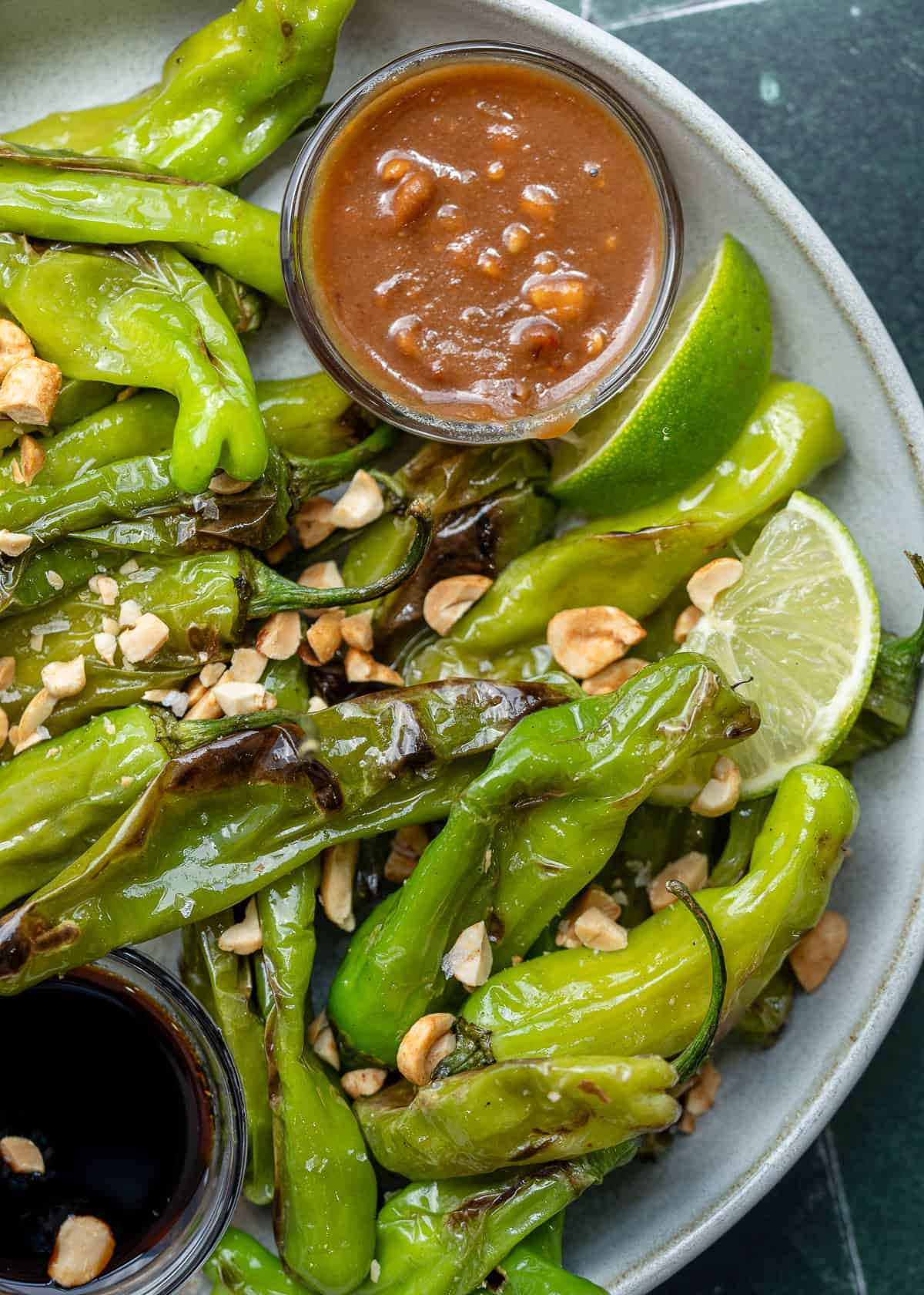 a plate full of perfectly blistered shishito peppers with peanut sauce